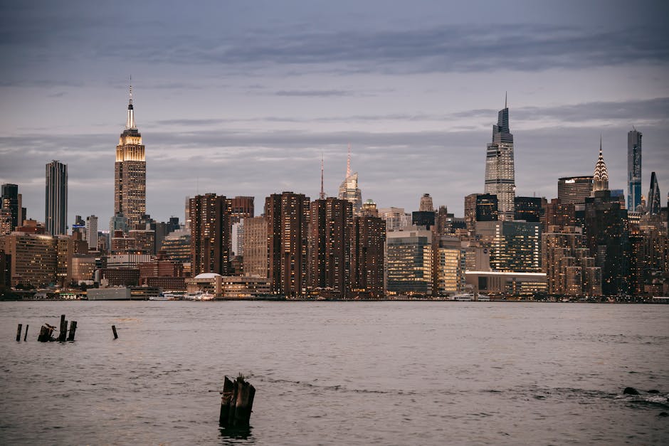 Modern architecture with towers and skyscrapers with luminous lights in windows on river bank in NYC