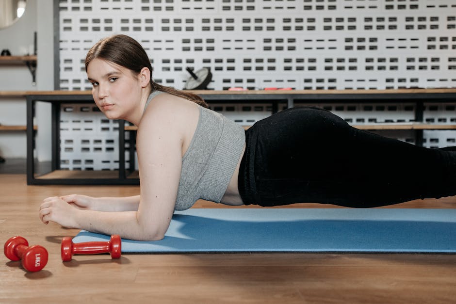 Woman doing planks on a yoga mat indoors with dumbbells showing dedication to fitness